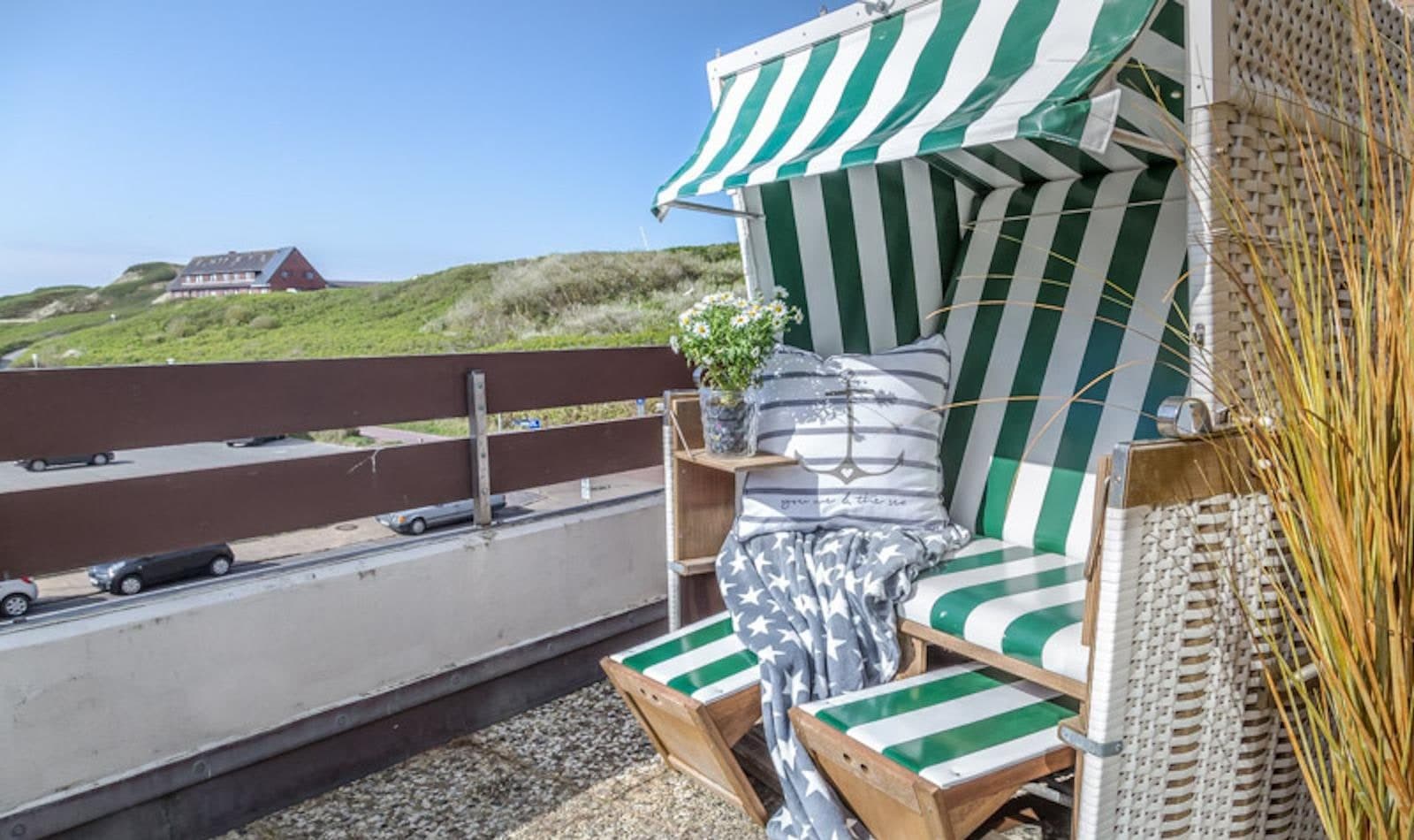 Südbalkon der Ferienwohnung in Westerland auf Sylt mit grün-weiß gestreiftem Strandkorb, Fußbänken und Blick über die Dünenkette