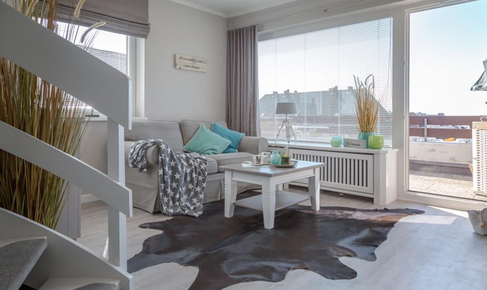 Wohnbereich mit großer Fensterfront und Balkontür, Sofa mit türkisen Kissen, Couchtisch und Fellteppich