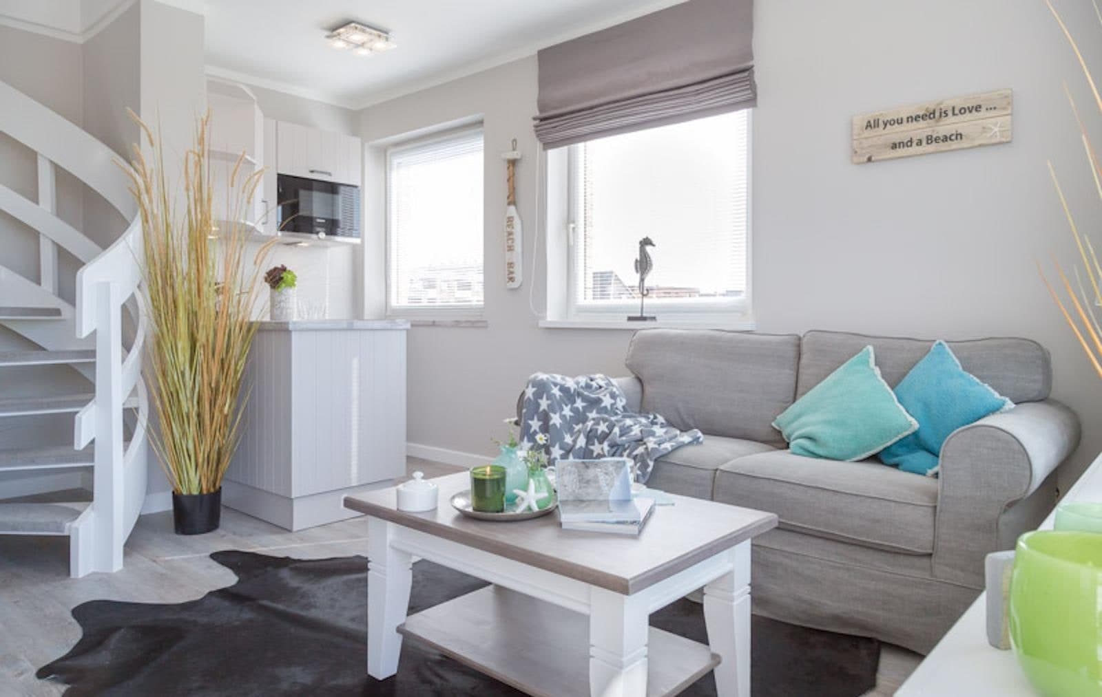 Helles Wohnzimmer der Ferienwohnung mit grauem Sofa, weißem Couchtisch und Fellteppich auf hellem Holzboden